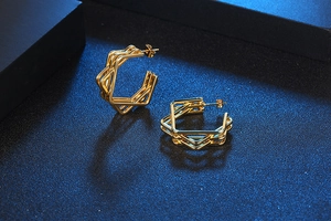 Macro shot of gold-plated multi-layer geometric hexagonal hoop earrings on blue texture
