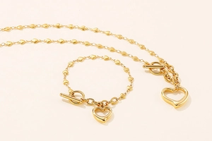 Detail of golden heart-shaped necklace and bracelet set with toggle clasp on beige background