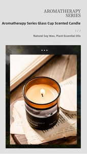 Cozy scene of lit soy wax candle in amber glass jar on wooden tray with vintage book