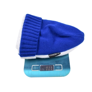 Blue and white knit beanie hat weighing 111g on a digital scale