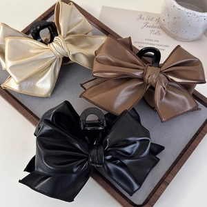 Set of three large faux leather bow hair claws in gold, brown and black on a wooden tray