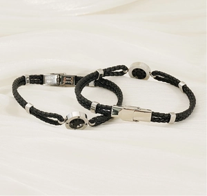 Close-up of compass anchor clasp on black braided leather bracelet with steel texture