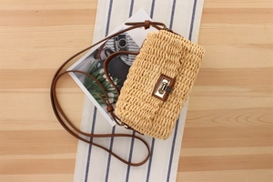 Close-up of woven straw bag with a metallic twist lock on light wood tabletop