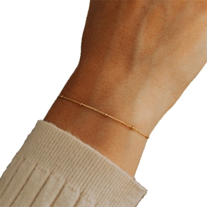 Minimalistisches goldenes Satellitenarmband mit kleinen Perlen am Handgelenk mit Strick