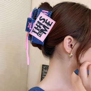 Detail of denim hair claw clip with pink 'THIS IS ME' patch on female model hairstyle