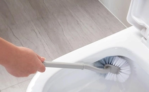 Detail of gray long-handle toilet brush cleaning the inner rim of a white ceramic toilet