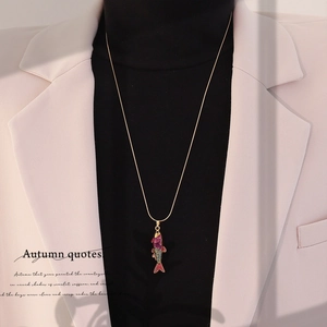 Detail of a purple koi fish pendant on a gold chain necklace worn over a white blazer