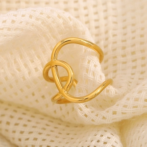 Cross knot open ring in 18K gold plated stainless steel on a textured background
