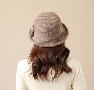 Detail of a brown houndstooth cloche hat with a ribbon bow on a female model
