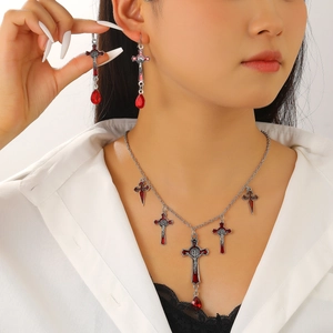 Detailed close-up of gothic silver cross necklace and earrings with red gemstone droplets