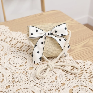Detail of straw crossbody bag with white polka dot bow on a lace tablecloth