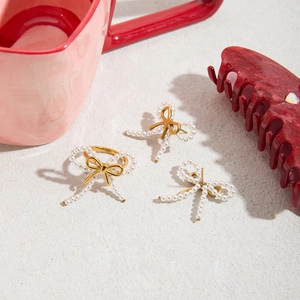 Detailed view of gold bow-shaped earrings and ring set with white imitation pearls
