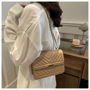 Model wearing a beige V-quilted shoulder bag with a metal chain strap over a white shirt