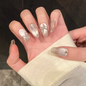 Dettaglio di unghie finte champagne argento cat-eye con farfalla 3D e catena metallica