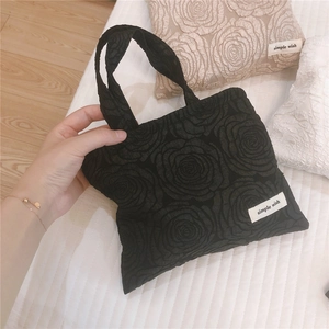 Detail of black mini tote bag featuring 3D rose texture and simple wish fabric label