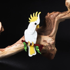 Handcrafted acrylic parrot brooch with white feathers and yellow crest on a wooden branch