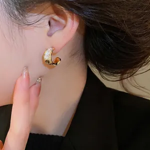 Elegant gold C-shaped earrings with white enamel and oval emerald green gemstone inlay