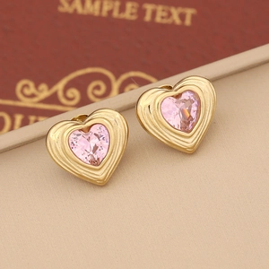 Macro shot of gold heart earrings with pink gemstones and wavy texture details