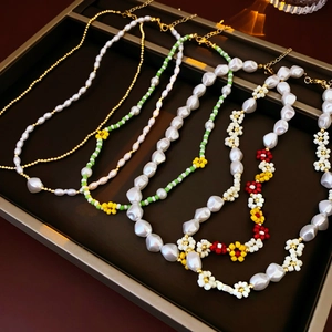 Flat lay of gold beaded, floral and baroque pearl necklaces in a dark display tray