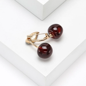 Detailed view of cherry brooch with red resin fruit and golden metal leaves on white stand