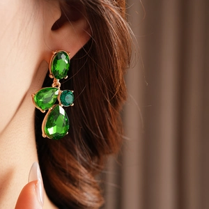 Close-up of vintage geometric teardrop earrings with green faceted crystals on a model