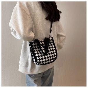 Detail of checkered knit tote bag featuring black handles and shoulder strap against beige wall