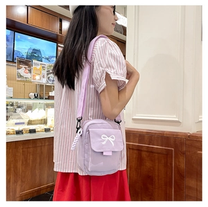 Detail of light purple crossbody bag with white bow and woven rope charm accessory