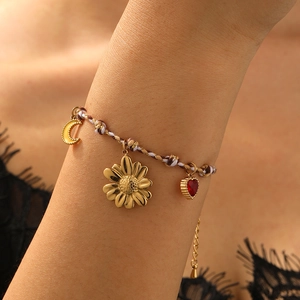 Bohemian braided rope bracelet with gold sun, moon, and red heart charms on woman's wrist