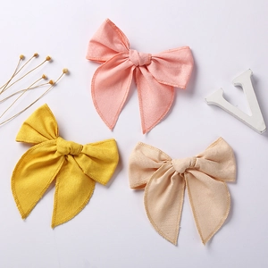 Close-up of three linen cotton bow hair clips in pink yellow and beige on white background