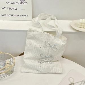 Detailed close-up of white sequined tote bag with silver metallic bow accents and lace fabric