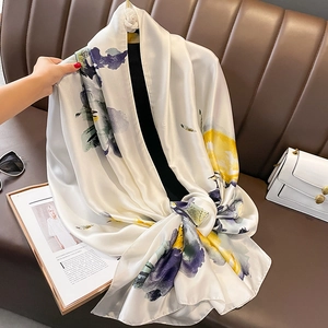Elegante sciarpa in raso avorio con motivo floreale drappeggiata su un divano in pelle