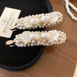 Detailed close-up of handmade pearl shell hair clips with golden vintage metal label