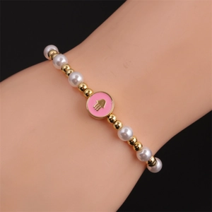 Detail view of a Hamsa Hand beaded bracelet with white pearls and pink enamel charm