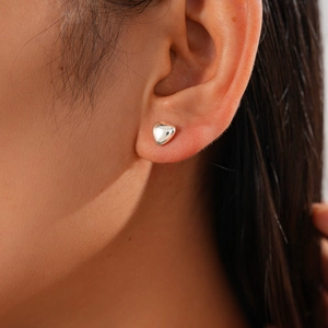 Detail showing a 3D puffy heart stud earring in silver finish on a model's earlobe