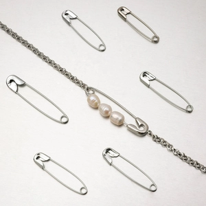 Silver chain bracelet with a large safety pin pendant featuring three white pearls on metal