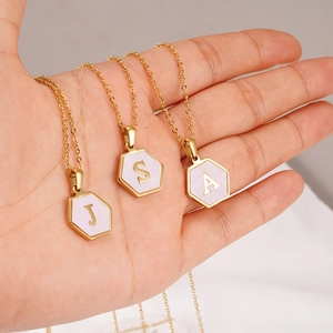 Gold hexagon necklace with pink shell inlay and engraved initials J, S, A held in hand