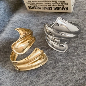 Detailansicht unregelmäßig gefalteter Armreifen in Gold und Silber auf grauem Textil