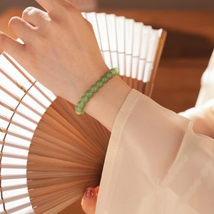 Detailed close-up of emerald green jasper beads bracelet worn with a traditional fan