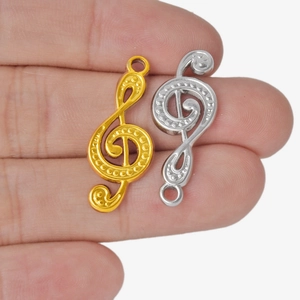 304 stainless steel G-clef music note pendants in gold and silver held on fingertips