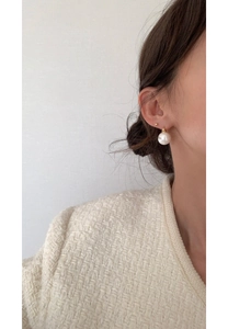 Detail of elegant white pearl drop earring and small gold stud worn by a model