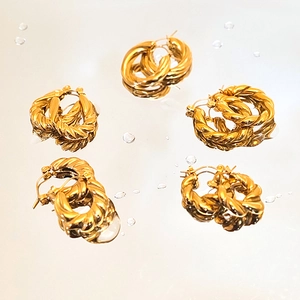 Detailed view of five pairs of golden twisted hoop earrings on a reflective mirror surface