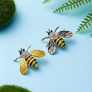 Close-up of alloy bee brooches with yellow enamel and sparkling rhinestones on mossy background