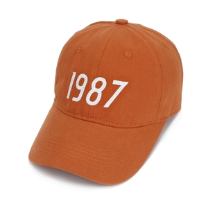Detail view of orange baseball cap with white 1987 embroidery and curved brim
