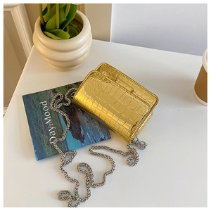 Macro detail of gold crocodile-patterned leather texture and metallic chain on handbag