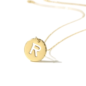 Close-up view of a gold-plated stainless steel circular pendant featuring a cutout letter R