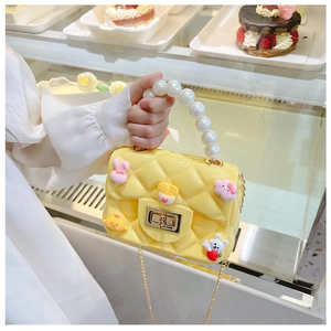 Detail of yellow quilted silicone bag featuring pearl handle and cartoon accessories