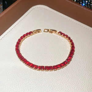 Macro shot of 18k gold ruby tennis bracelet with square cut red gemstones on leather