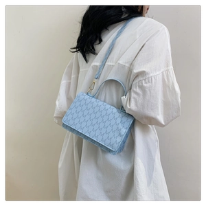 Detail of light blue crossbody bag with monogram pattern on a model in white shirt