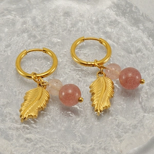 Boho golden feather earrings with pink beads on a textured glass tray for women