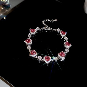 Detailed view of silver heart bracelet with pink zircon stones on reflective black base